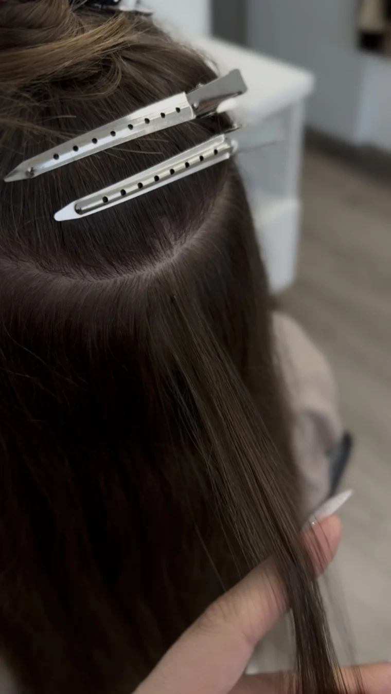 Plaukų priauginimo korekcija atliekama grožio salone Femin Manifest – profesionali meistrė dirba su priaugintomis sruogelėmis.